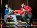 Man in blue top sitting next to man in red jacket in A Strange Loop
