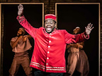 An actor in a red bell hop suit with his arms up in A Strange Loop