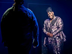 An actor in silhouette taking to an actor at the back of the stage in A Strange Loop