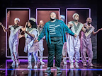 An actor in a green shirt with other actors behind him in purple in A Strange Loop