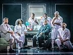 An actor in a green short sitting in the middle of other actors in purple in A Strange Loop