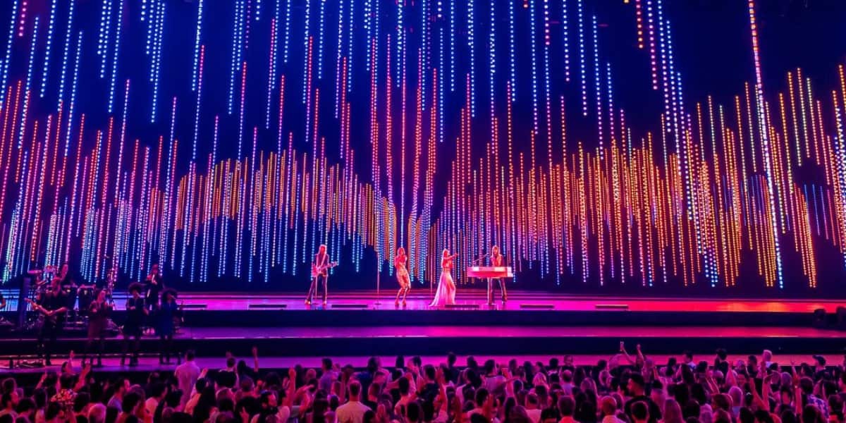 Dynamic light show and digital avatars at the ABBA Voyage arena, viewed from the crowd.