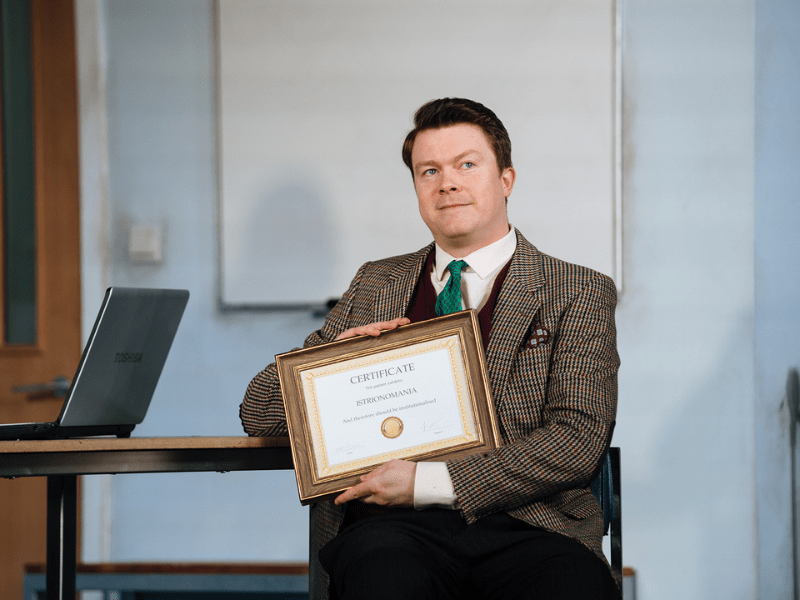 Man in a suit and tie sat at a desk holding a certificate