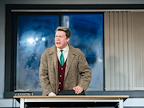Man in suit and tie stood behind a desk shouting