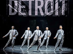 The Temptations dancing in grey suits in front of a Detroit sign