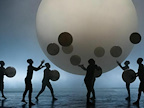 Image: Gandini Jugglers, shadowed figures juggling shadowed balls in-front of a large white orb.