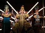 Image: Katie Stevenson, Anthony Roth Costanzo and Rebecca Bottone stood on stage in different regal outfits. 