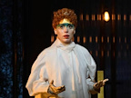 Image: Rebecca Bottone wearing a white robe, with green makeup across her eyes and her hands out.