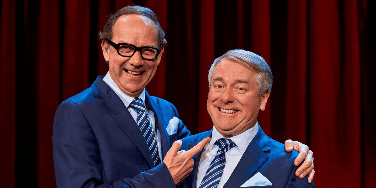 Two men smiling, one wearing glasses from An Evening of Eric and Ern 
