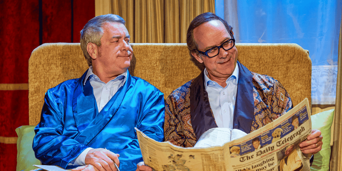 Two men sitting on a couch in dressing ropes with one reading the newspaper from An Evening of Eric and Ern 