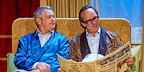 Two men sitting on a couch in dressing ropes with one reading the newspaper from An Evening of Eric and Ern 