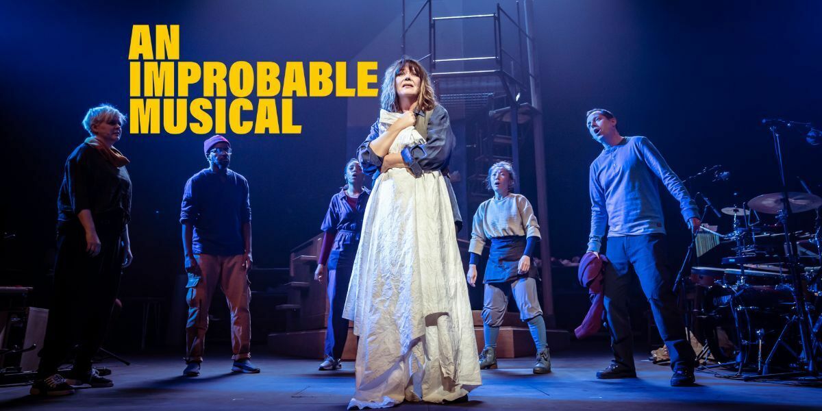 Text: An Improbable Musical in bold yellow block writing.  Image: a woman stands in the middle of a stage with a spotlight on her, she is surrounded by men and women and cradles a large white sheet. She has a hopeless look on her face. The stage lighting is navy.