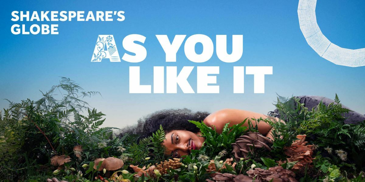  Text: Shakespeare's Globe, As You Like It. Image: a woman laying in forrage - leaves, twigs and mushrooms looking at the camera with a smirk on her face. She is against a blue sky.