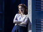 Woman leaning on wall next to a shuttered window.