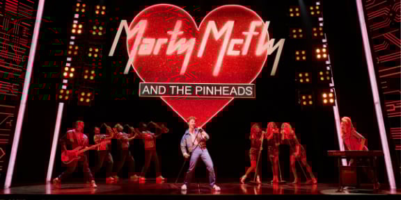 Back To The Future The Musical in London. Marty is performing with his band, Marty McFly and the Pinheads. The band name is hanging above them on a lit-up heart.