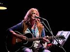 Woman seated playing guitar and singing.