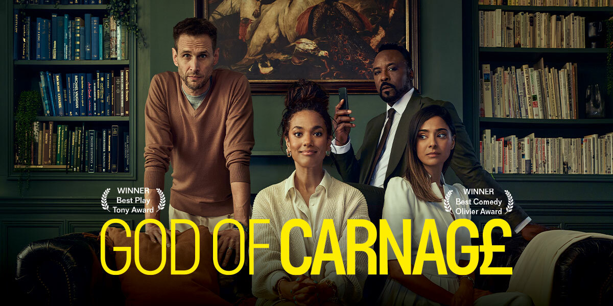 Text: God of Carnage. Image: Two women sat on a sofa, one looking straight forwards and the other looking to her right. Behind them two men are standing, one wearing chinos and a jumper and the other in a suit and tie holding a mobile phone.