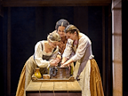 Mhairi Gayer (Tilly),  Madeleine Mantock (Agnes) Frankie Hastings (Eliza) and stand over a bowl, using their hands and smiling. They are all dressed in corsets and skirts in shades of yellow, grey and brown.  Photo by Manuel Harlan © RSC
