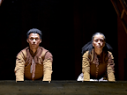 Ajani Cabey (Hamnet) and Alex Jarrett (Judith) lean over the edge of a wooden ledge, both are dressed in brown and green and look concerned.  Photo by Manuel Harlan © RSC