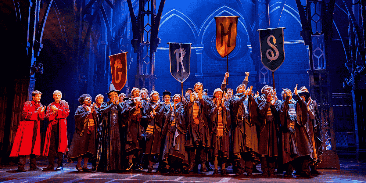 Image: Hogwarts students cheer while holding their house banners Show: Harry Potter and the Cursed Child 