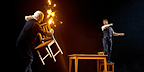 Image: Two wizards as one casts a fire spell with a wand and the other raises a chair to defend himself Show: Harry Potter and the Cursed Child