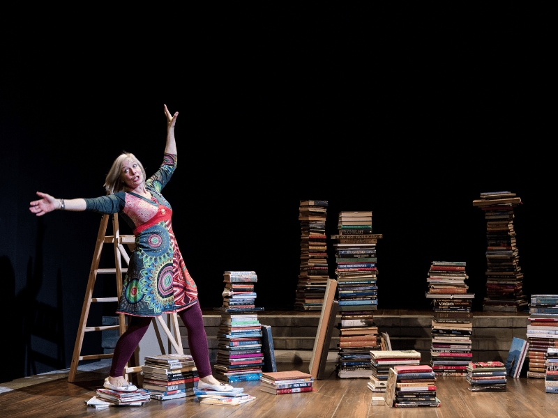 Danyah Miller on a stage surrounded by piles of books and a step ladder.