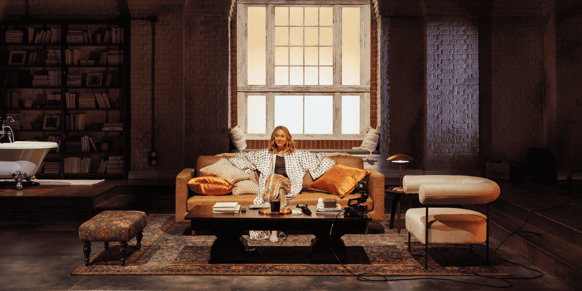 Show: Interview at Riverside Studios Image: A woman seated on a sofa in her living room, facing toward the stage.