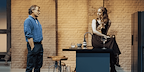 Show: Interview at Riverside Studios Image: Two people in the living kitchen counter as one sits on the counter top and engage in conversation.