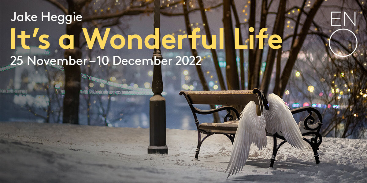 Jake Heggie It's a Wonderful Life 25 November - 10 December 2022 ENO. A snowy park overlooks the lights of the city. A pair of angel wings hang on the back of the snow dusted park bench.