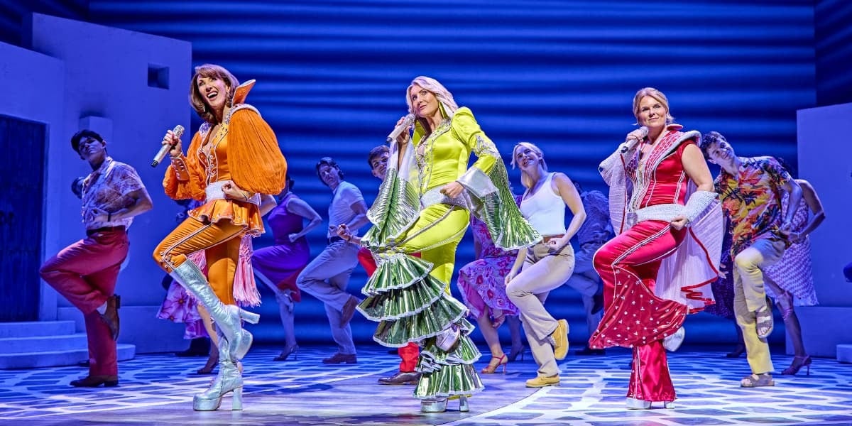Donna and the Dynamo's each wear a brightly coloured flared jumpsuit whilst dancing