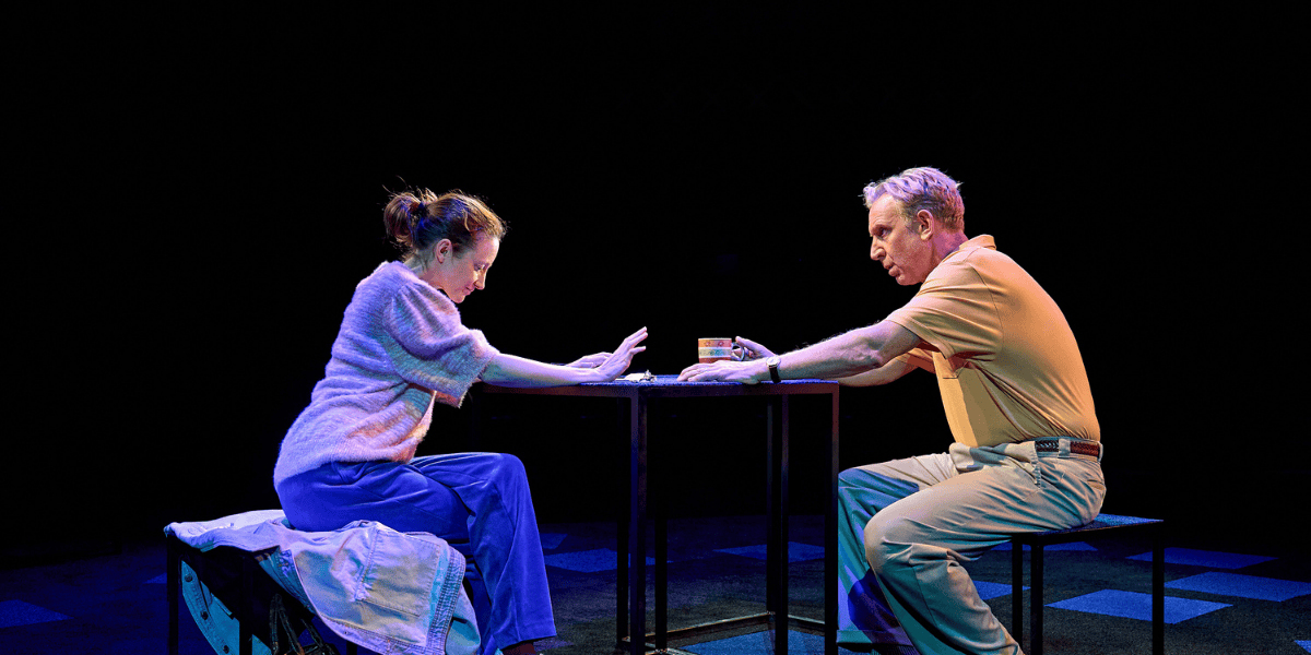 Man and woman sitting down with their hands on the table in Mary Page Marlowe