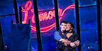 Christian and Satine share a tender embrace in front of a glowing sign during Moulin Rouge! The Musical at the Piccadilly Theatre.