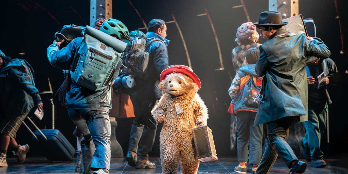 Paddington surrounded by actors in a lively stage scene, from the West End show.