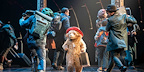 Paddington surrounded by actors in a lively stage scene, from the West End show.