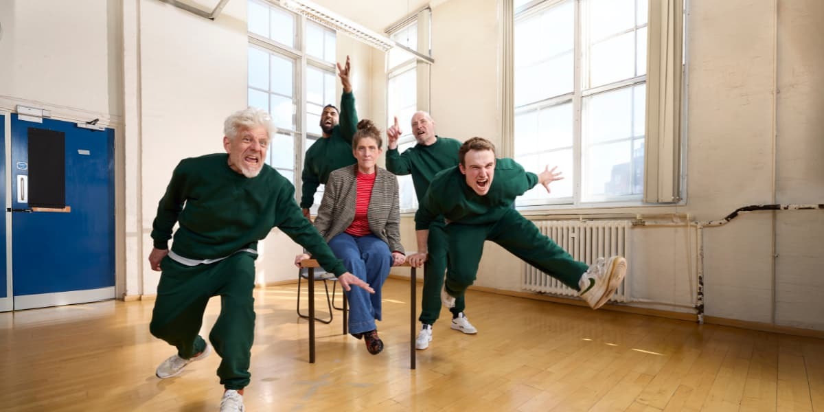 Penned Up. A Woman sits on a chair, four men in green tracksuits surround her jumping and yelling 