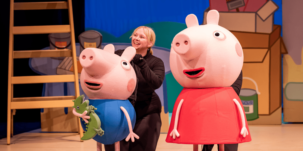 Small pig with blue top holding a dinosaur alongside bigger pig in red dress from Peppa Pig's Big Family Show!