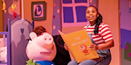 Woman in dungarees and stripped top reading a book to a pig from Peppa Pig's Big Family Show!