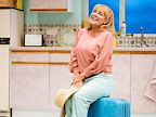 Sheridan Smith in Shirley Valentine - sat on a blue suitcase in  a kitchen holding a straw hat in her hand.