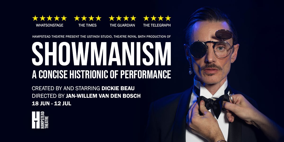 Showmanism. A man in a suit has his bowtie adjusted by a pair of hands. One lens of his sunglasses is up, he is looking at the camera