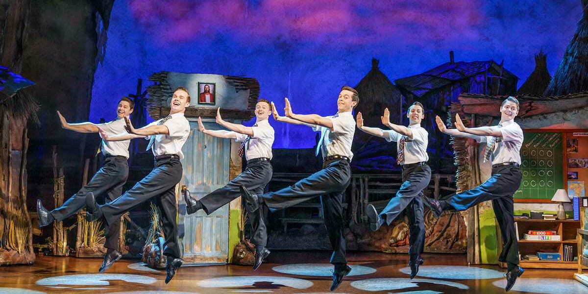 A group of missionaries in white shirts and ties perform a lively dance number in the Book of Mormon musical.