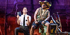 Elder Price kneels holding the Book of Mormon while facing a local warlord in the London stage production.