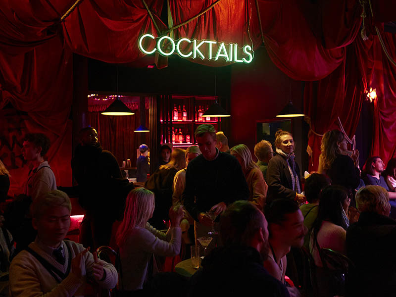 Crowded cocktail bar with a neon Cocktail sign.