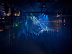 Crowd stood around a staircase bathed in blue light whilst multiple people are on the staircase in various poses.