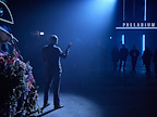 Man stood facing away from camera gesturing to onlookers stood under a neon Palladium sign.