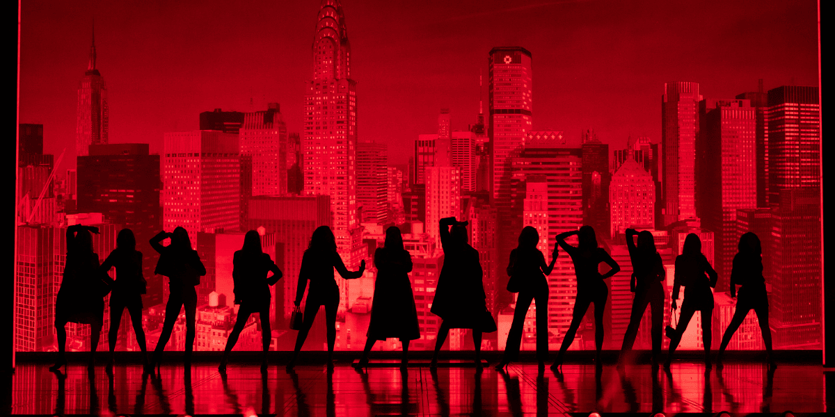 Des acteurs en silhouette se dressent sur un décor rouge audacieux de la ville lors d’une scène d’ensemble saisissante dans The Devil Wears Prada London.