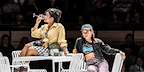 Two women from The Lady From the Sea sitting one a table and one drinking from a wine glass. 