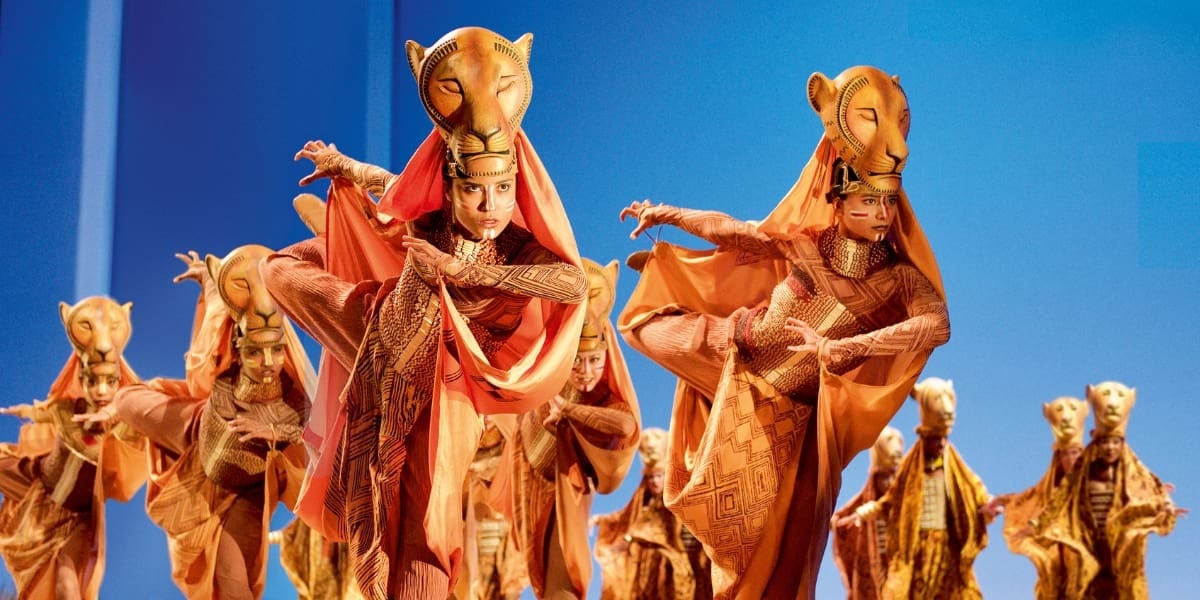 Lionesses move across the stage in a powerful ensemble scene from The Lion King London, wearing striking animal-inspired costumes.