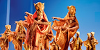 Lionesses move across the stage in a powerful ensemble scene from The Lion King London, wearing striking animal-inspired costumes.