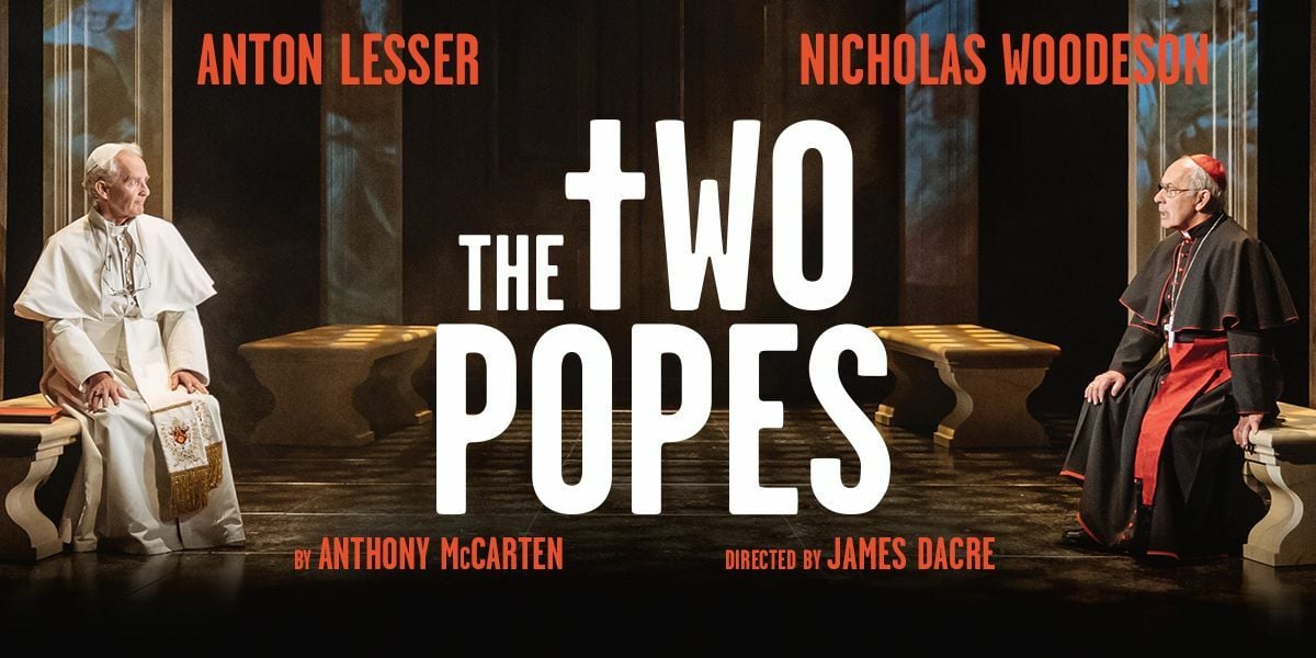 Text: Anton Lesser. Nicholas Woodeson. The Two Popes. By Anthony McCarten. Directed by James Dacre. | Image: In a gallery with projected images on the walls, there are benches on either side of the room. There is a pope on the left in white dress robes and a pope on the right in black and red dress robes. 