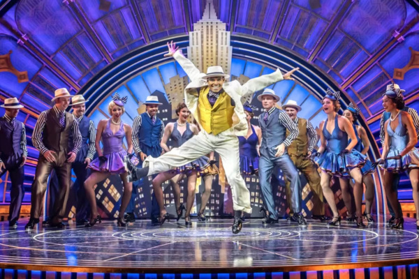 Dancers perform a glamorous 1930s routine in Top Hat, with a lead performer leaping centre stage in a white suit.